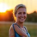 Una donna sorride mentre fa stretching al tramonto, simboleggiando il raggiungimento di obiettivi di benessere.